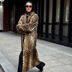 Fashion influencer @sobalera in London wearing a chic winter outfit with a knit triangle head scarf, a leopard print faux fur coat, oval sunglasses, black pants, and loafers.