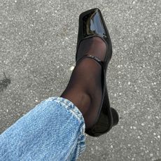 Woman wears black patent Mary-Janes, sheer socks, and blue jeans.