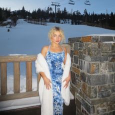 Sabrina Carpenter posing in front of a ski lift wearing a blue snowflake dress and fairy dust eye shadow.