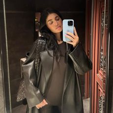 Kylie Jenner wears a brown leather jacket, a brown bodysuit, and a brown bottega veneta bag.