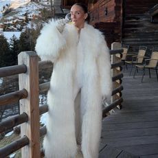 Emma wears a white fur coat, white ski suit, and white moon boots.