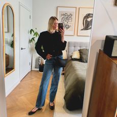 Natalie Cantell takes a mirror selfie in her apartment in New York, wearing a classic outfit: Reformation Val jeans, a Harris Tapper cropped black collarless blazer, flat black J. Crew sling-back shoes, and carrying a black Celine Croque bag.