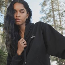 Woman wearing black alo yoga jacket with trees in background