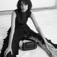 Black and white photo of woman sat on floor with black bag