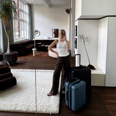 Fashion editor Natalie Cantell with Away suitcases taking a mirror selfie at The Rental by Ellison Studios in Sydney, wearing a Toteme ribbed racerback tank, the Harris Tapper Irving Trousers, Toteme croc effect brown flip flop sandals.