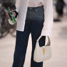 a photo of a woman carrying a designer Gucci Jackie handbag in white with blue jeans, and a white button-down shirt